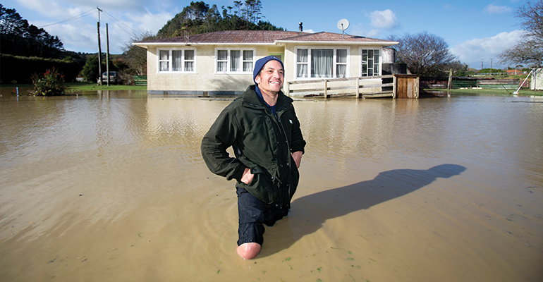 A man standing outside his house in knee-high water