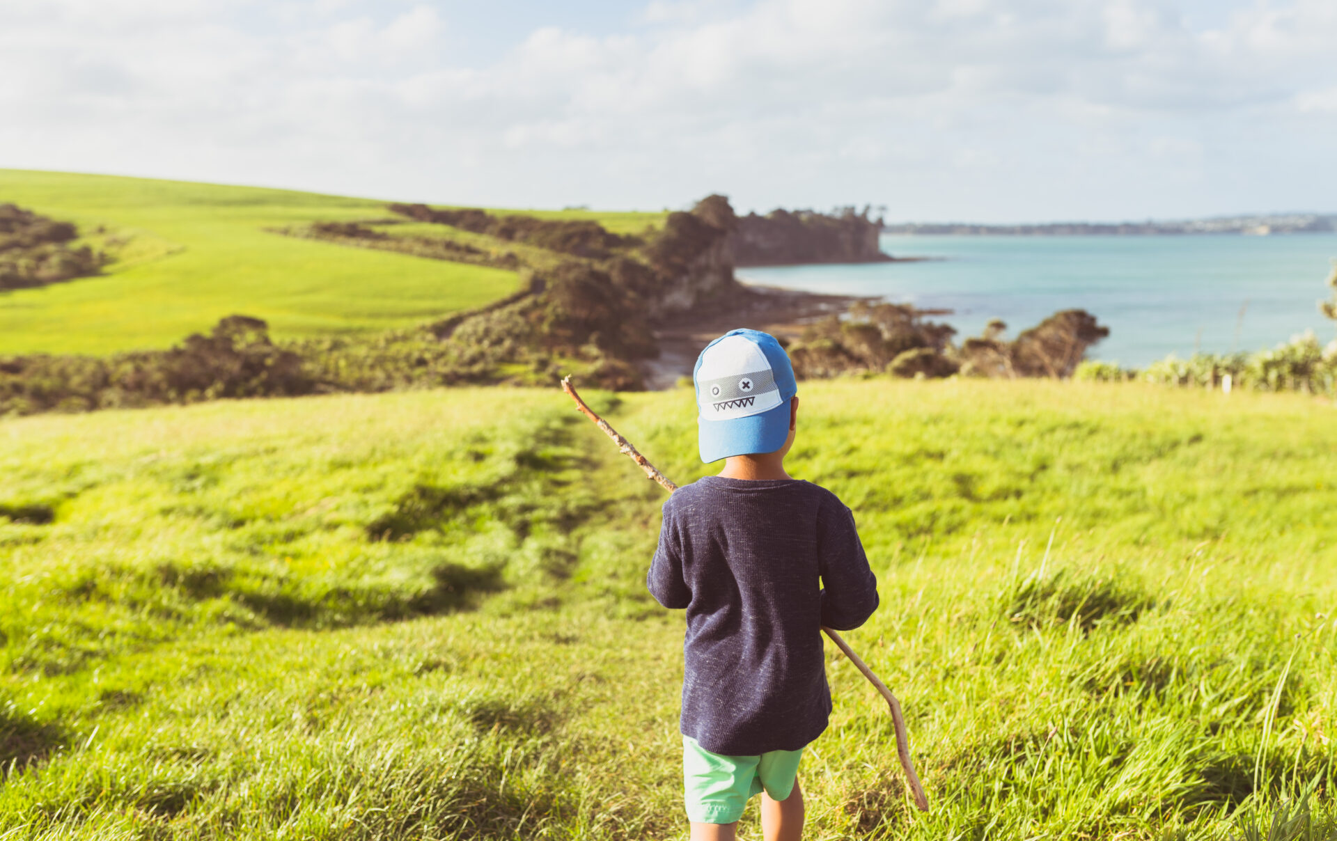 A child stands in a grassy field with the ocean in the distance