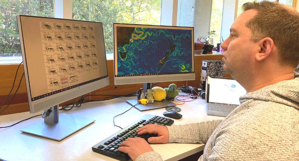 A person sits at desk with two screens showing climate modelling